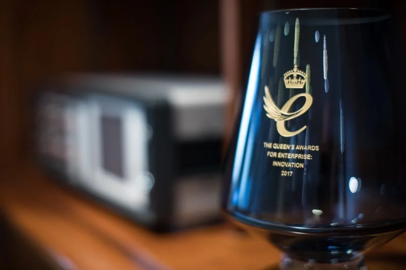 A blue glass Queen's Award for Enterprise trophy engraved 'The Queen's Awards for Enterprise: Innovation 2017', with a microK instrument visible out of focus behind it.