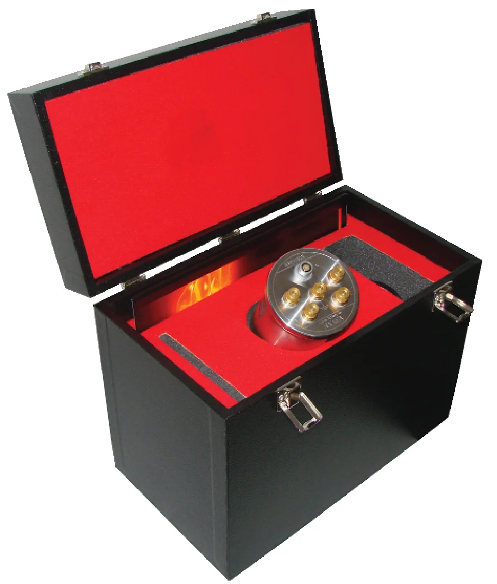 A cylindrical resistance bridge calibrator standard in stainless steel and red, seated in the red felt-lined interior of its black transit case, with six gold-plated connectors visible on its top face and the case lid open.